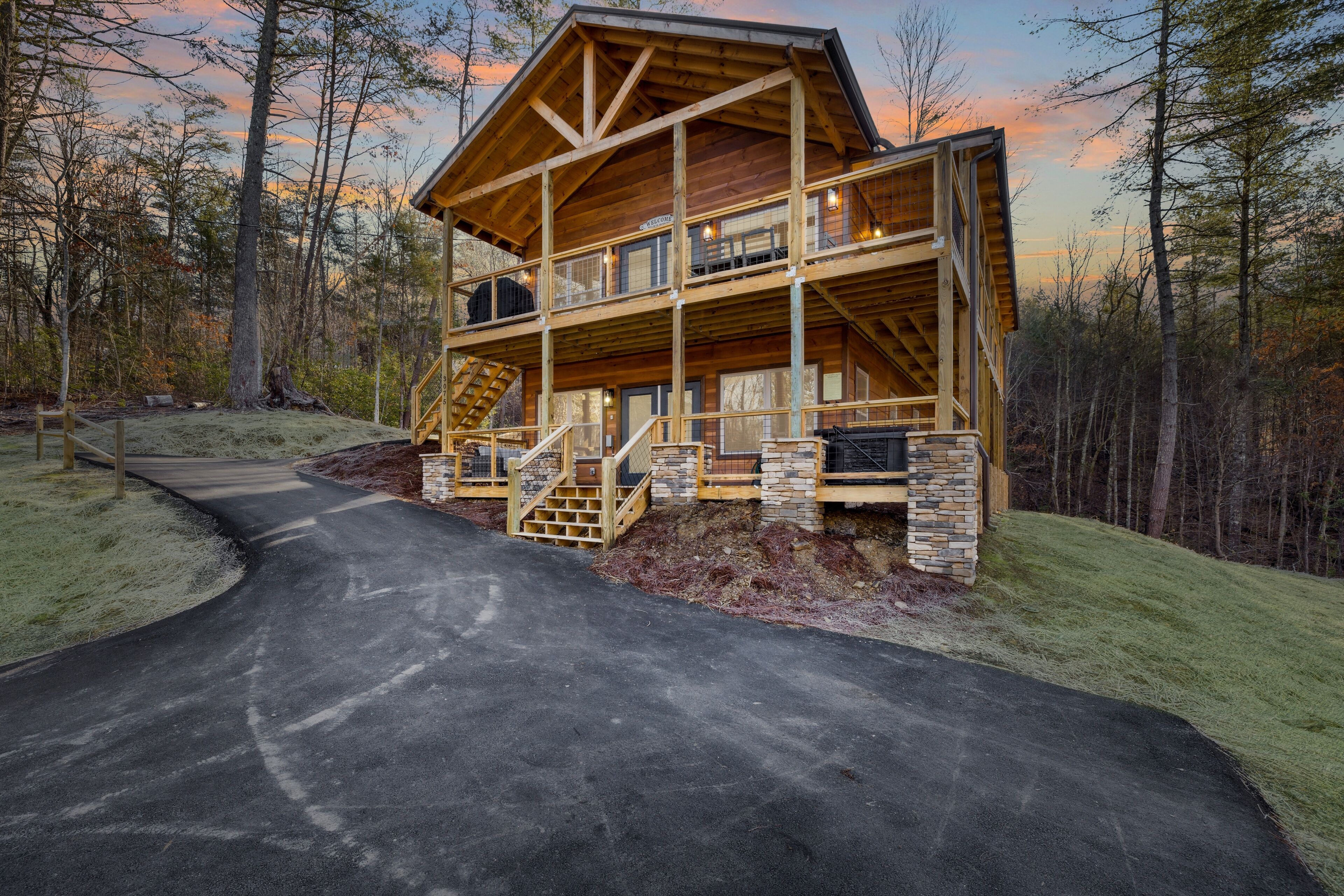 A two-story log cabin with a stone foundation, a covered porch, and a staircase leading to the upper level.