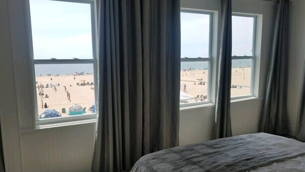 Une chambre à coucher avec un lit, deux fenêtres et vue sur une plage.