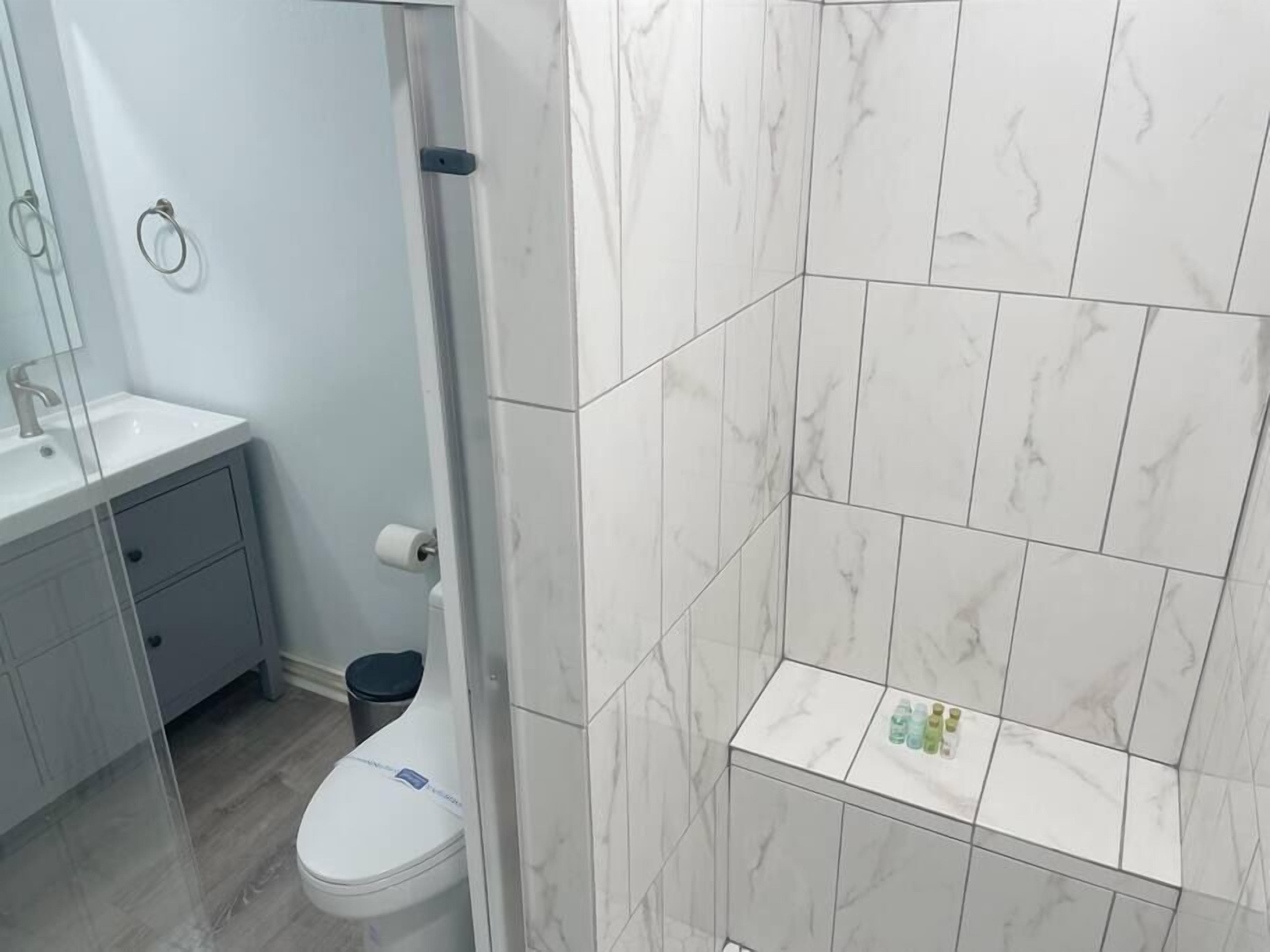 Une salle de bain avec des toilettes blanches, un lavabo et un espace douche dont le mur est recouvert de carreaux de marbre.
