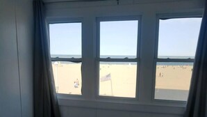 Une chambre avec un lit, une fenêtre à trois carreaux et une vue sur une plage où flotte un drapeau américain.