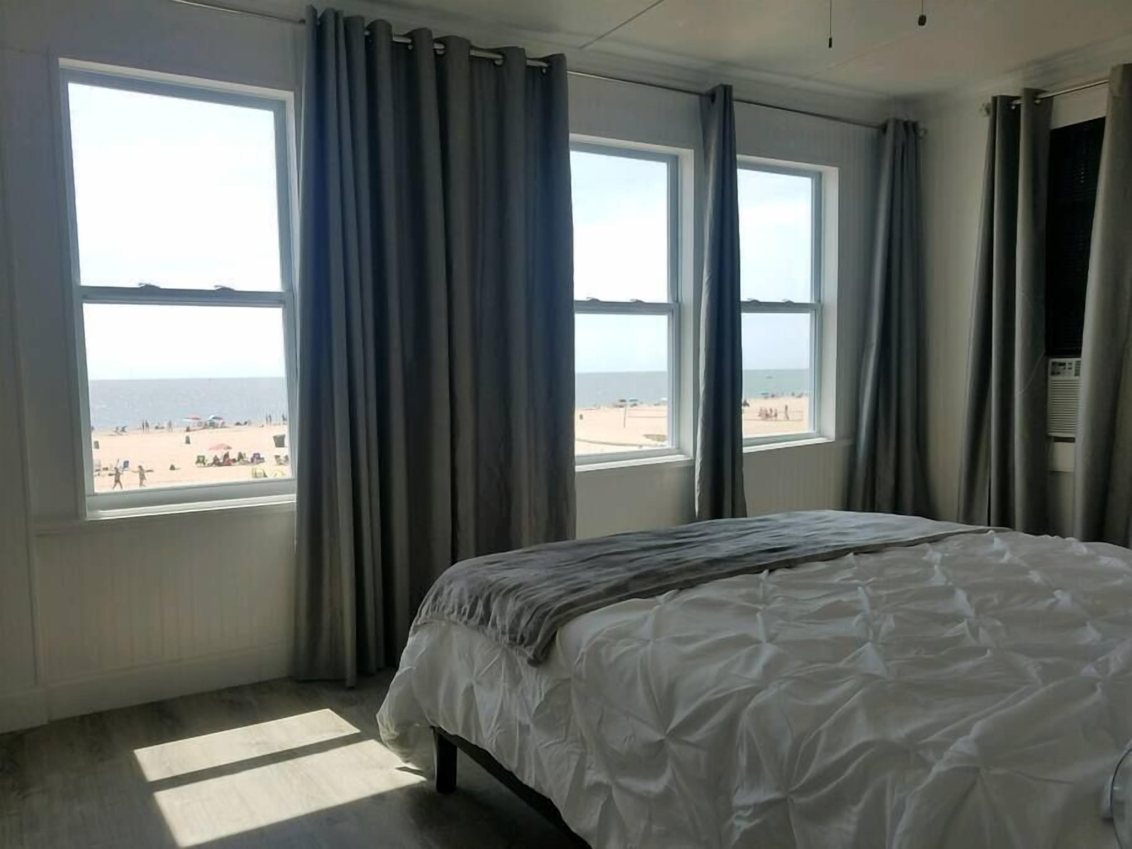 Ein Schlafzimmer mit Bett, großen Fenstern und Blick auf den Strand.