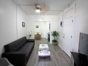 Een woonkamer met een bank, een bijzettafeltje, een plant en een tv-meubel.