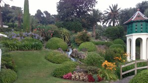 A garden with a small waterfall, neatly trimmed bushes, and a gazebo.