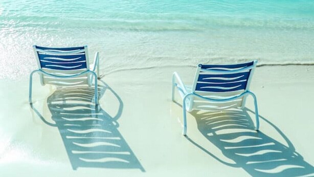 Deux transats sur une plage de sable fin, avec une eau turquoise et cristalline.