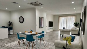 Un salon moderne comprenant un coin repas, des canapés blancs, une table basse agrémentée d’une plante et une horloge murale.