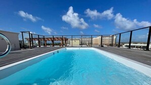 Une piscine sur le toit, avec un ciel bleu dégagé et des bâtiments qui se dressent au loin.