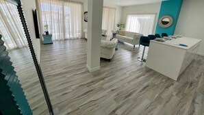 Una sala de estar moderna con un sofá blanco, un comedor con una mesa blanca y una escalera con peldaños color turquesa.