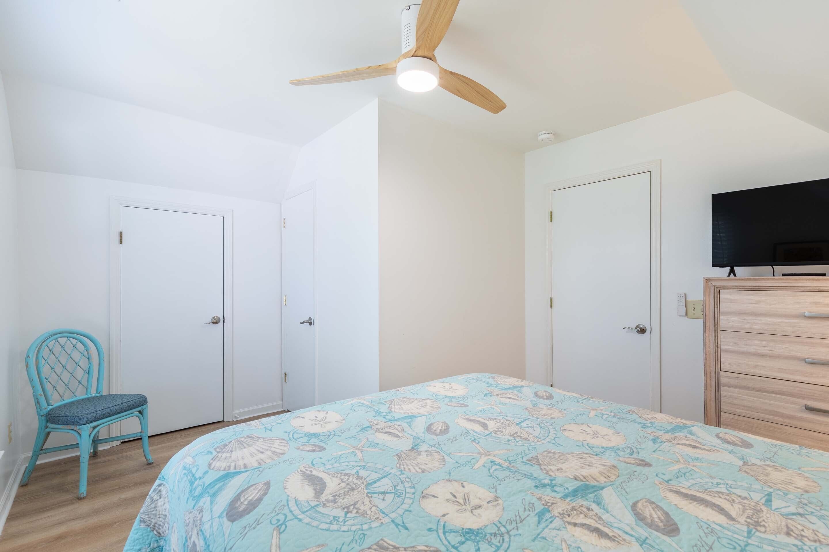 A bedroom with a bed, a ceiling fan, a TV, and a dresser.