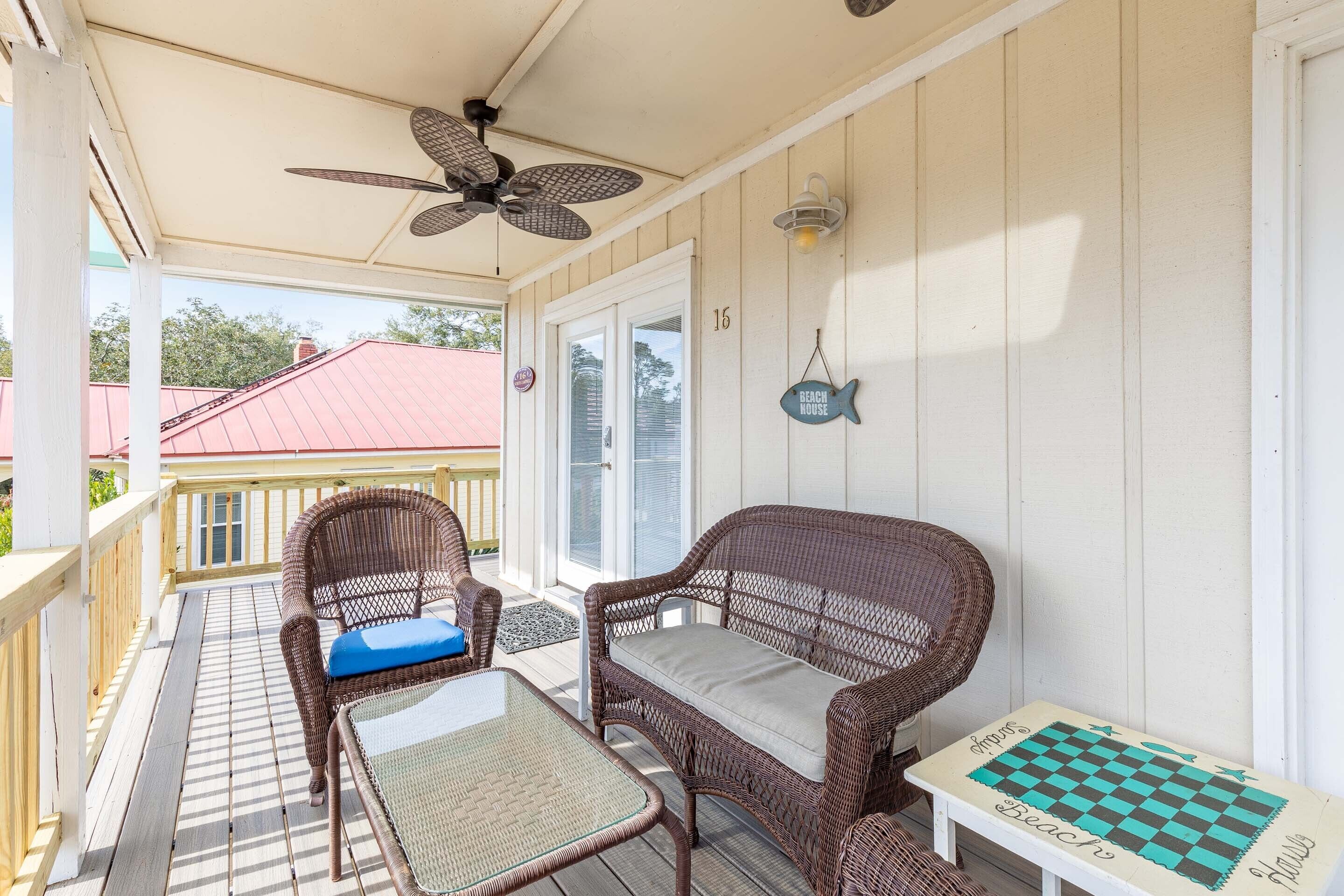 A covered porch with wicker furniture, a ceiling fan, and a small table with a chessboard.