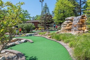 A miniature golf course with a green artificial turf, a waterfall feature, and a variety of trees and shrubs. - In home Games, Gym, & Movie Room+FREE Pool Access! (McGaheysville)