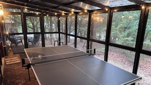Et bordtennisbord i et rum med store vinduer, klinkegulv og lyskæder.