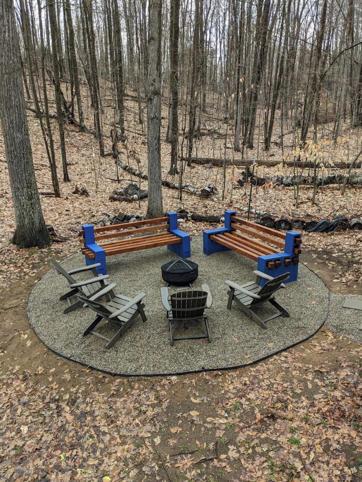 Un espace extérieur circulaire aménagé avec des bancs et des chaises, un foyer et un sol en gravier.