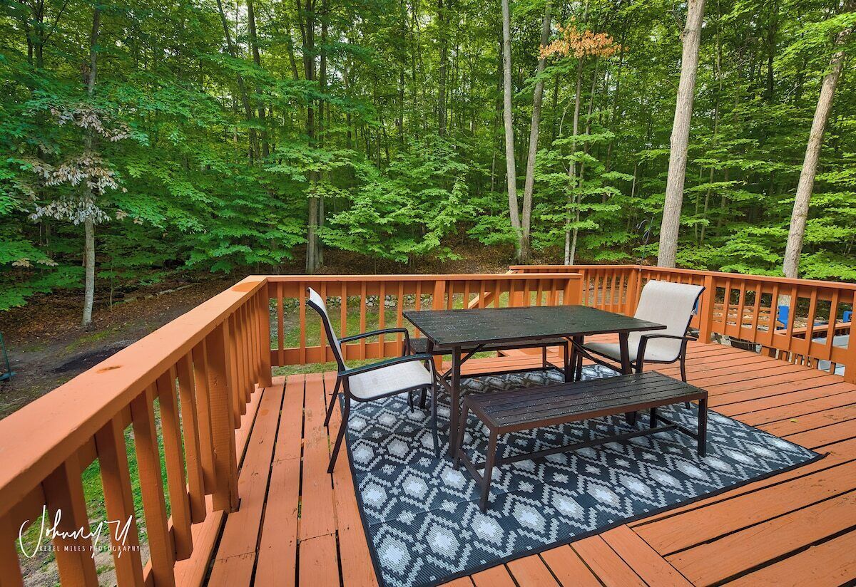 A wooden deck with a table and chairs, surrounded by a forest.