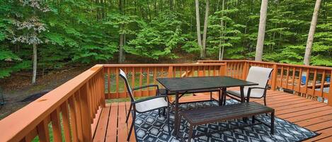 A wooden deck with a table and chairs, surrounded by a forest.