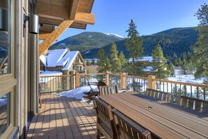 Una terraza de madera con una mesa y sillas, con vista a un paisaje nevado que incluye casas y montañas.
