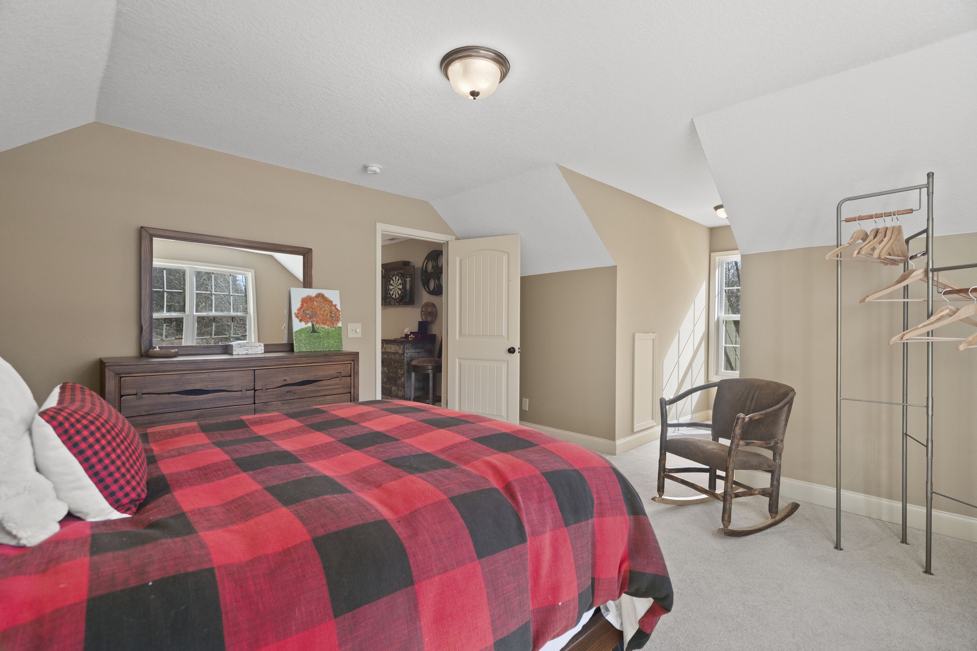 A bedroom with a large bed, dresser, rocking chair, and a clothing rack.