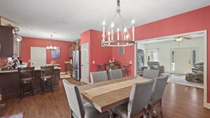 A dining area with a wooden table and six chairs, a chandelier, and a kitchen in the background. - Summer Snow: Large Pet-Friendly Family Home w Yard, Firepit | 6 Min to Downtown (Highlands)