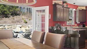 A dining area with a table and chairs, a kitchen with wooden cabinets, and a stone wall outside. - Summer Snow: Large Pet-Friendly Family Home w Yard, Firepit | 6 Min to Downtown (Highlands)