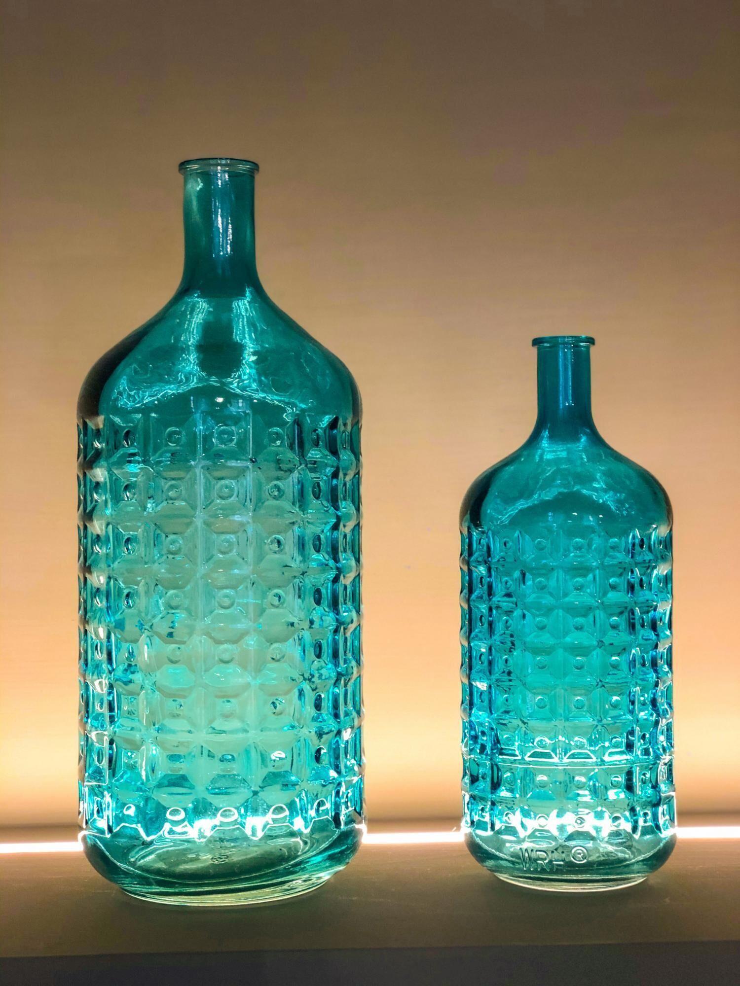 Two glass bottles with a textured pattern, placed on a flat surface against a plain background.