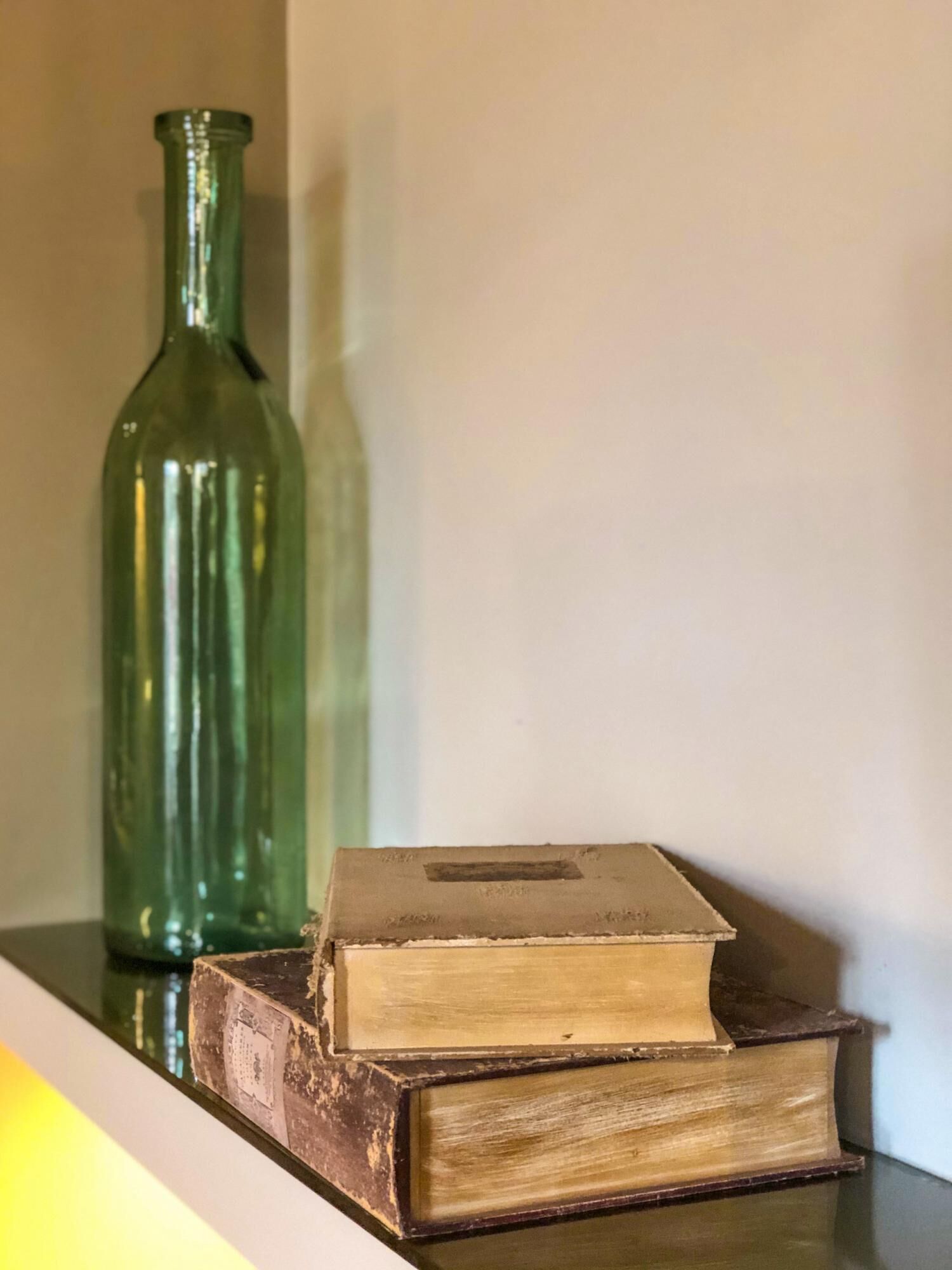 Una botella de vidrio verde y dos libros antiguos sobre una estantería.