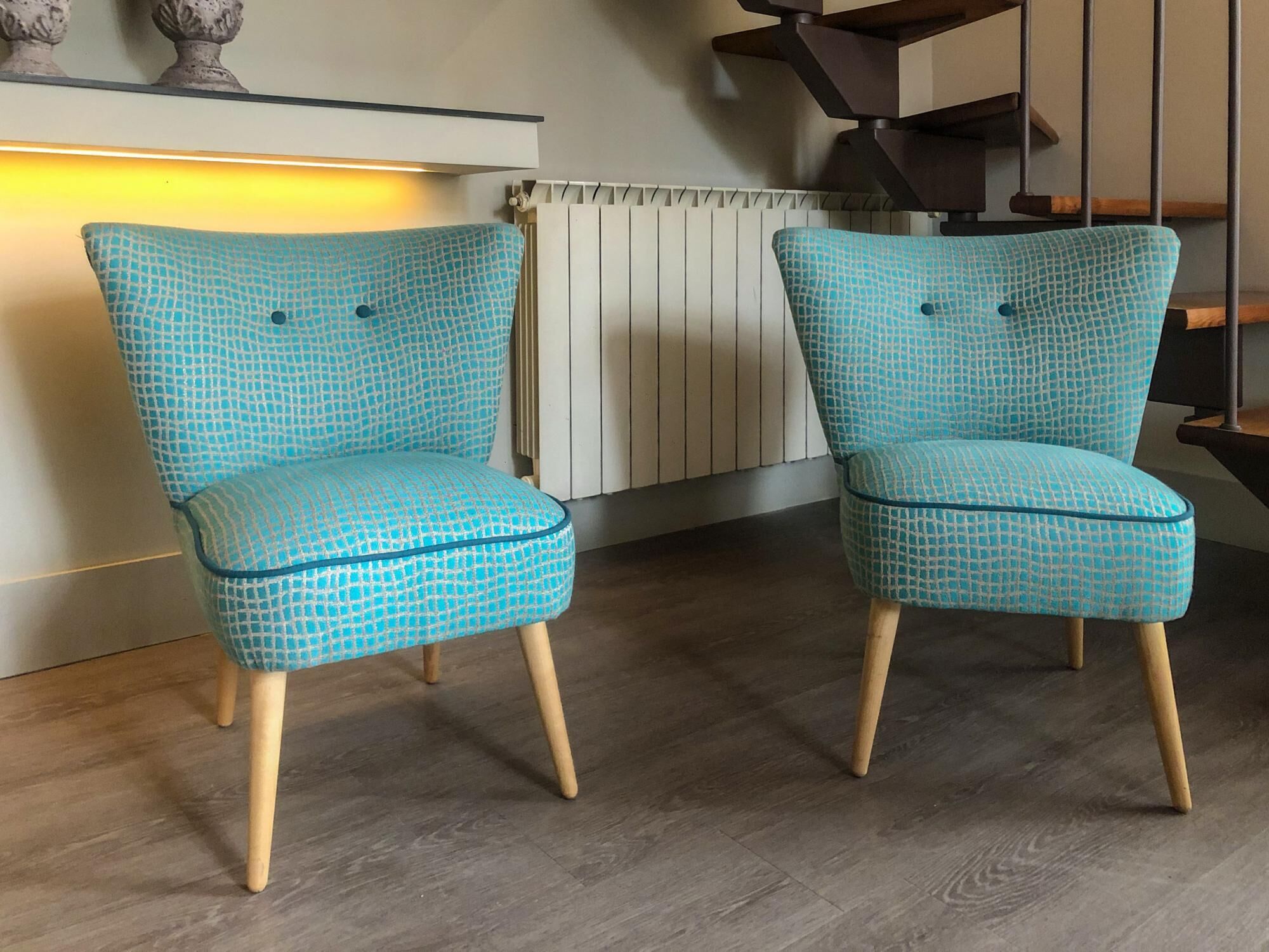 Dos sillas con estampado azul verdoso y patas de madera en una habitación con suelo de madera y un radiador blanco.