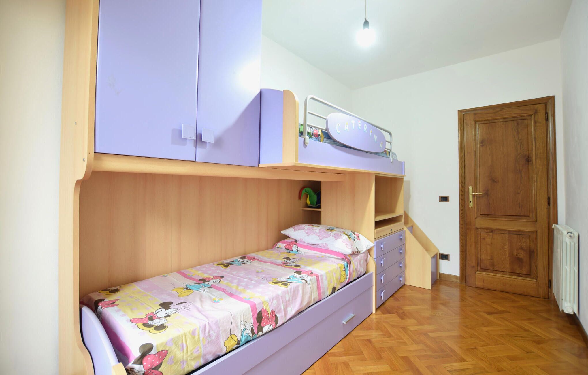 Un lit superposé avec un lit en bas et un lit en haut. Il y a une petite étagère sous le lit du haut et une porte sur la droite.