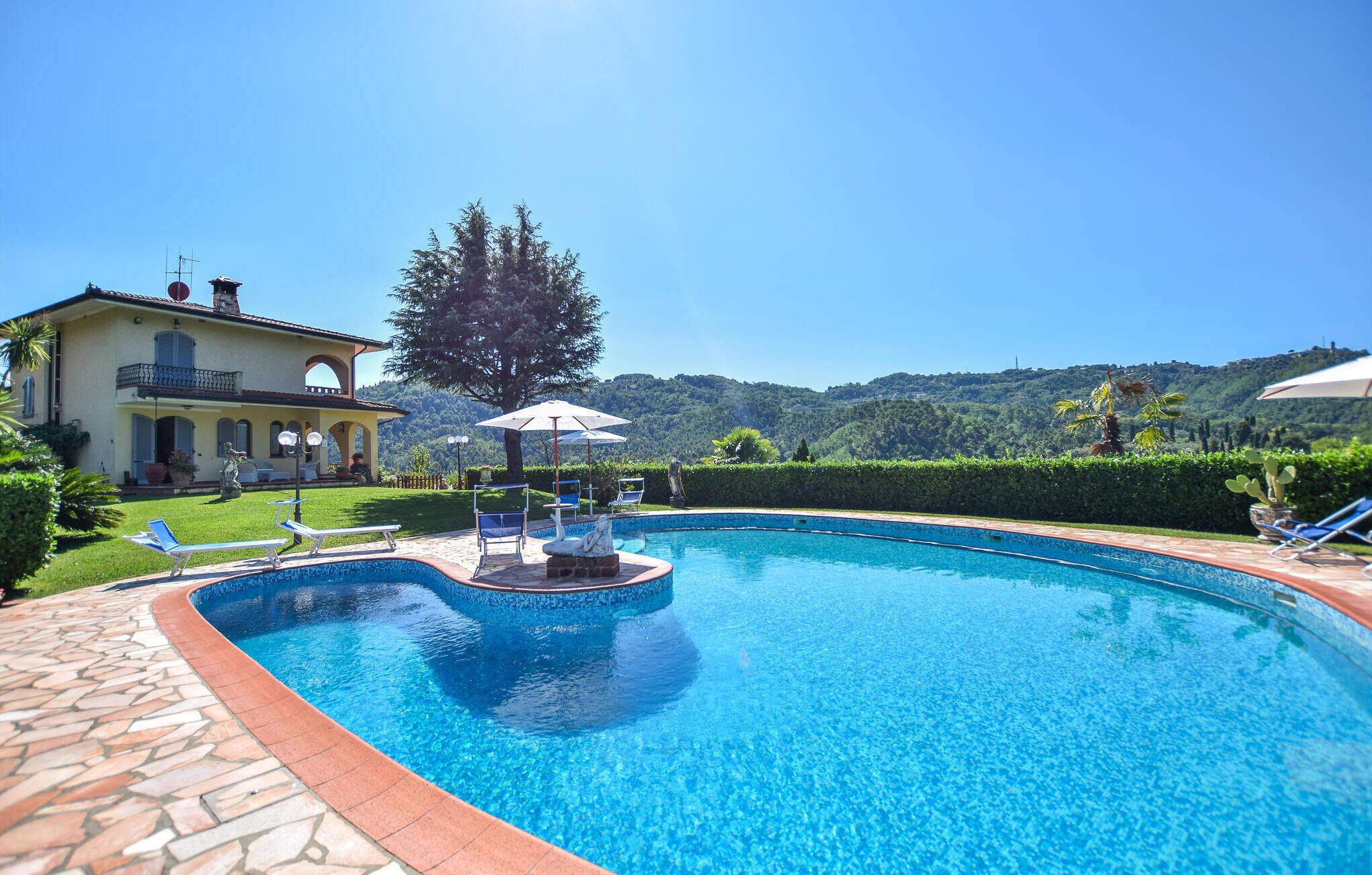 Uma piscina com borda de pedra, cadeiras de descanso e guarda-sóis.