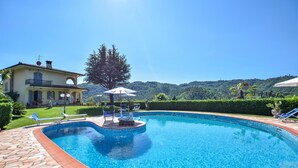 Une piscine bordée de pierres, avec des chaises longues et des parasols.