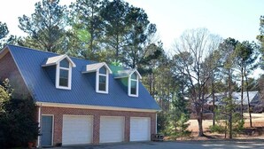 A two-story house with a blue metal roof, two garage doors, and a front yard with trees. - Cozy, 1-bedroom apartment, 11 miles to campus (Oxford)