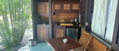 Un espace extérieur abrité, doté d’une table et de chaises en bois, d’un petit coin cuisine et offrant une vue sur la verdure.