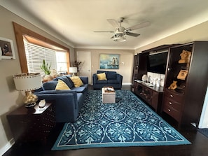 Ein Wohnzimmer mit blauem Sofa, einem gemusterten Teppich, einem Deckenventilator und einem Fernsehschrank.