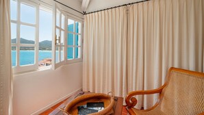 Une pièce avec vue sur la mer, une chaise en osier et une fenêtre avec des rideaux.