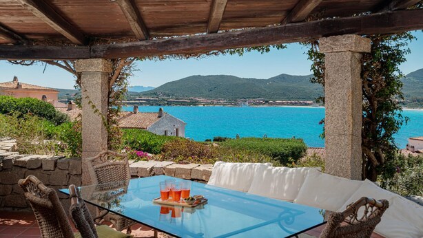 Un espace extérieur abrité, doté d'une table en verre, de chaises en osier et offrant une vue sur la mer et les montagnes.