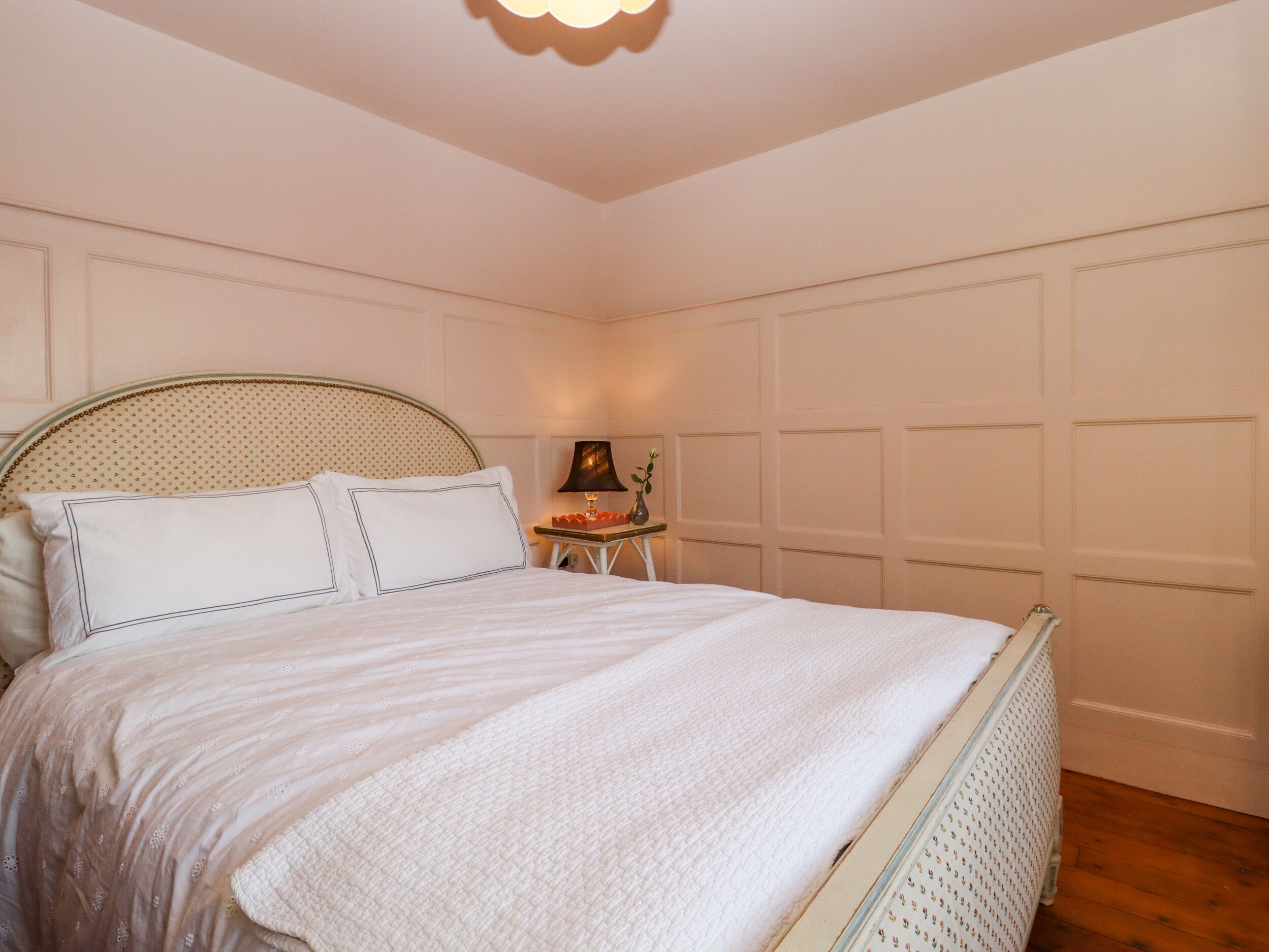 Un letto rifatto con un copriletto bianco e cuscini, un comodino con una lampada e un pannello decorativo al muro.