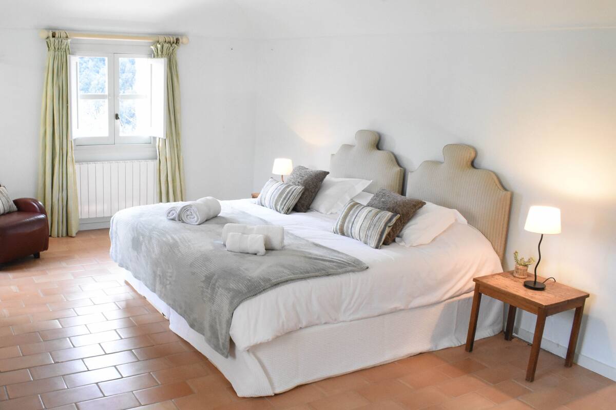 A bedroom with a large bed, a bedside table with a lamp, and a chair.