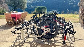 Een fietsenrek met meerdere fietsen geparkeerd op een betonvloer, een tafel met stoelen, en een bergachtig landschap op de achtergrond.