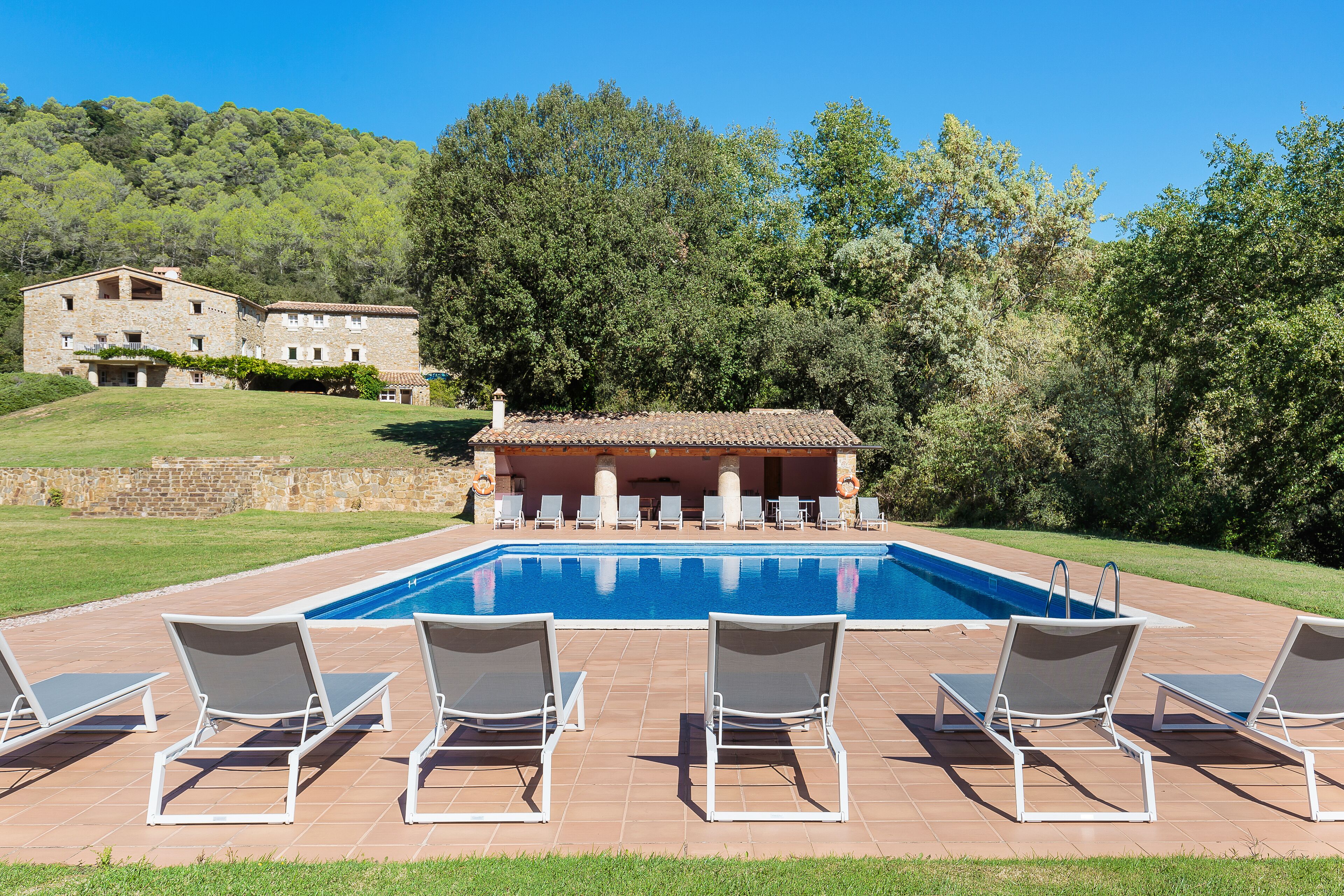 Una piscina con sillas de descanso, un edificio de piedra y un paisaje con colinas al fondo.