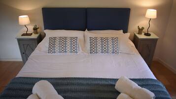 A neatly made bed with two pillows, two bedside tables with lamps, and two rolled towels on the bed.