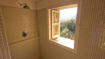 A bathroom with mosaic tile walls, a shower, and a window with a view of a forested landscape.