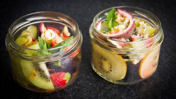 Deux bocaux en verre contenant une salade de fruits avec des tranches de kiwi, des fraises et des feuilles de menthe.