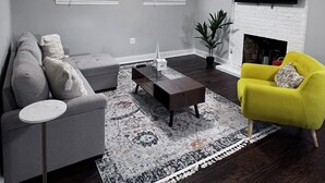 A living room with a grey sofa, a yellow armchair, a coffee table, and a fireplace. - Alexandria VA spacious, family-friendly 5BR Home near DC (Alexandria)