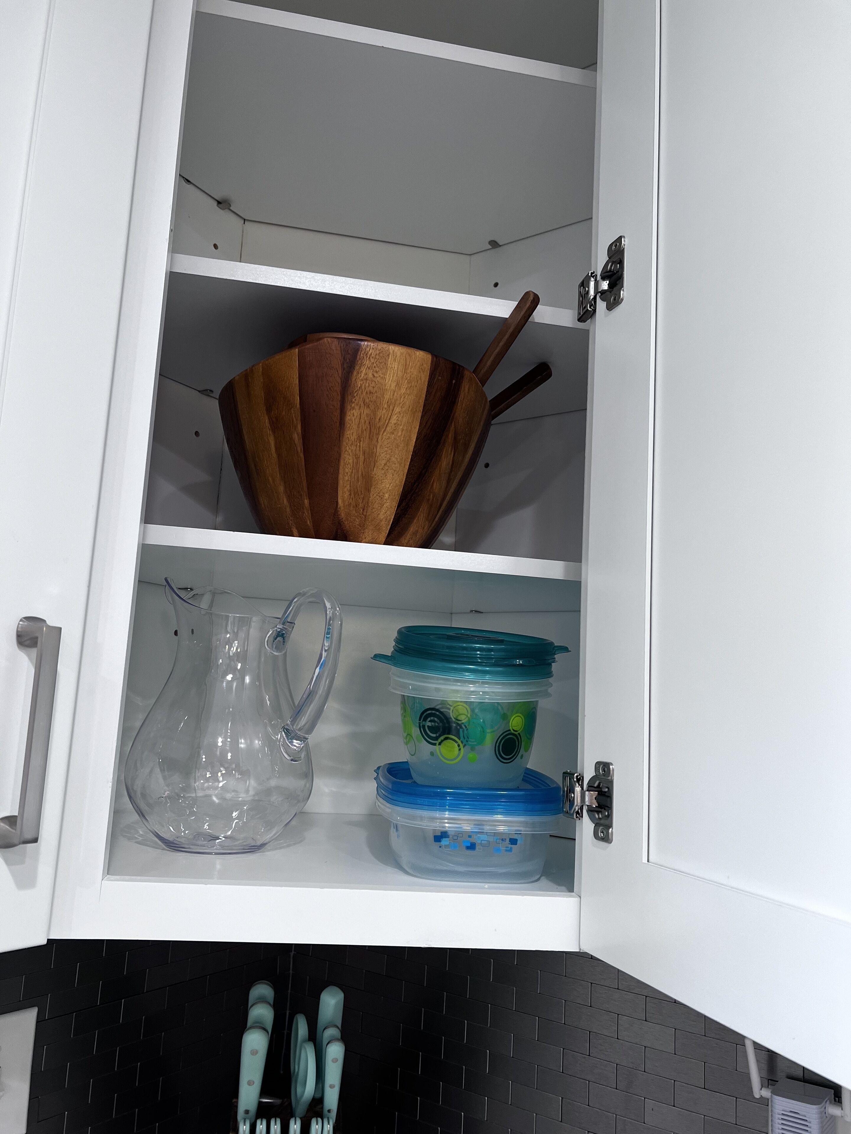 A kitchen cabinet with a wooden bowl, a clear pitcher, and two plastic containers with lids.
