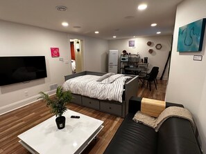 Een kleine woonruimte met een bed, een bank, een televisie, een kitchenette en een eethoek.