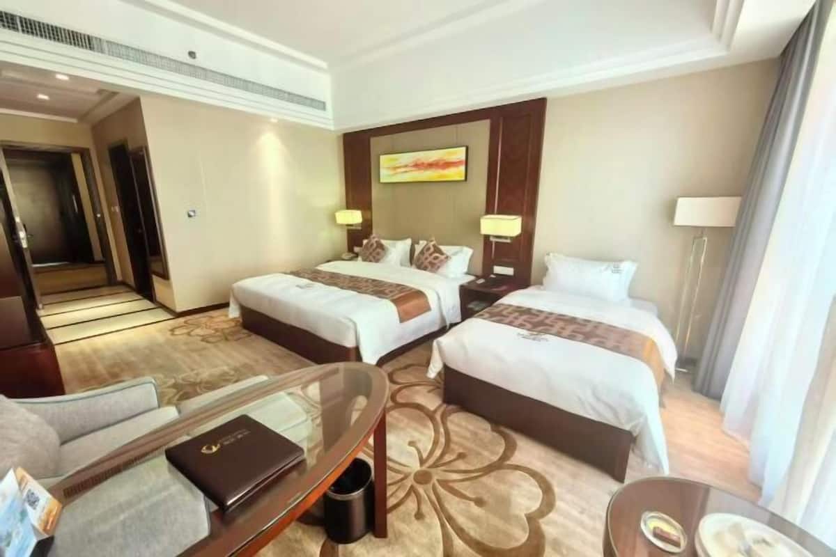 A hotel room with two beds, a desk, a chair, and a small table.
