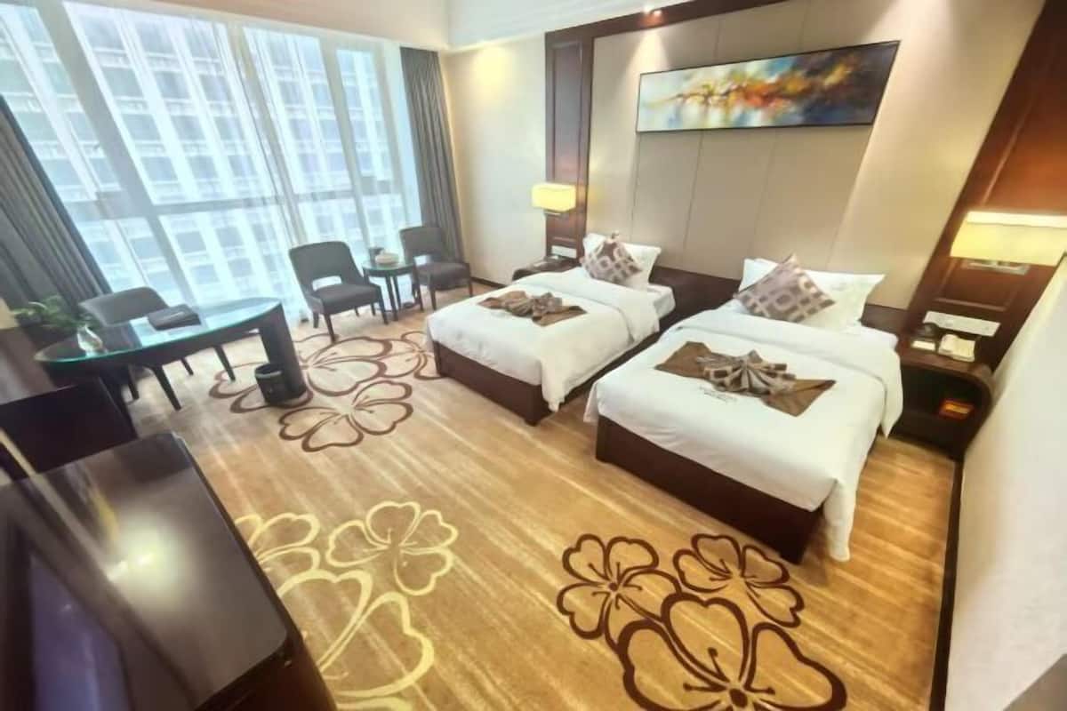 A hotel room with two beds, a desk, chairs, and a large window.