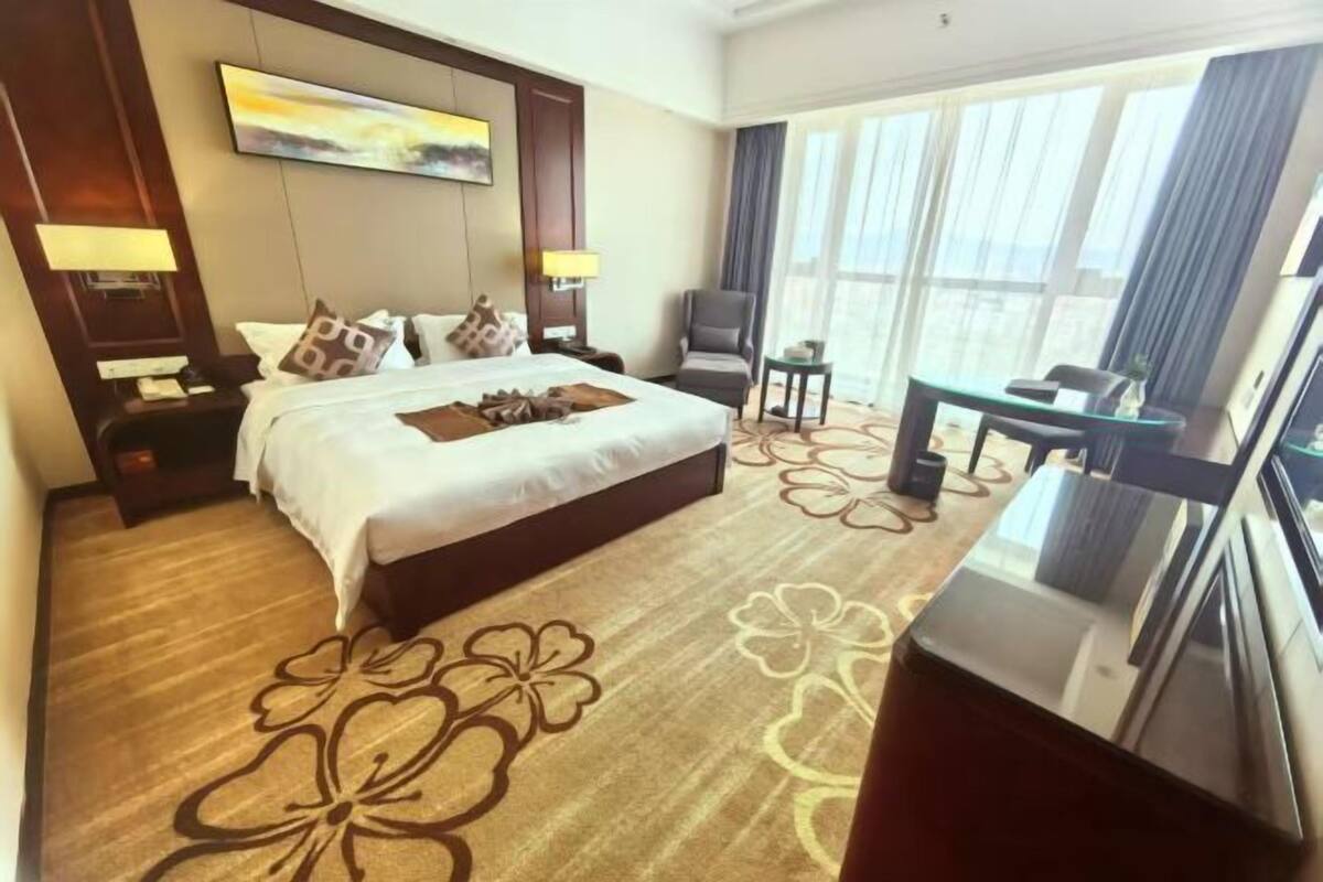 A hotel room with a large bed, a desk, a chair, and a view of the outdoors.