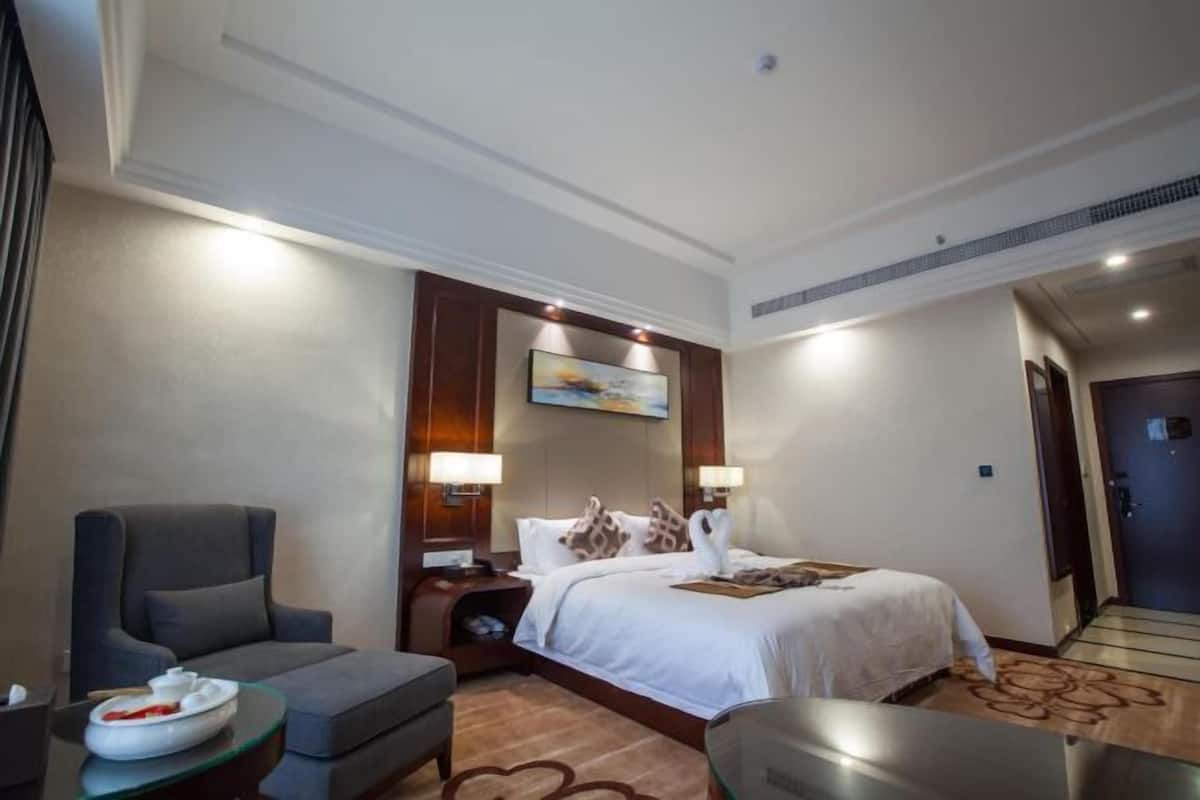 A hotel room with a bed, a sofa, a desk, and a painting on the wall.