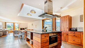 A modern kitchen with wooden cabinetry, a built-in oven, and a large island with a sink. - Beautifully presented Cotswold holiday cottage with a hot tub - Walnut Barn (Great Tew)