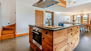 A modern kitchen with a central island, wooden cabinetry, and a built-in oven. - Beautifully presented Cotswold holiday cottage with a hot tub - Walnut Barn (Great Tew)