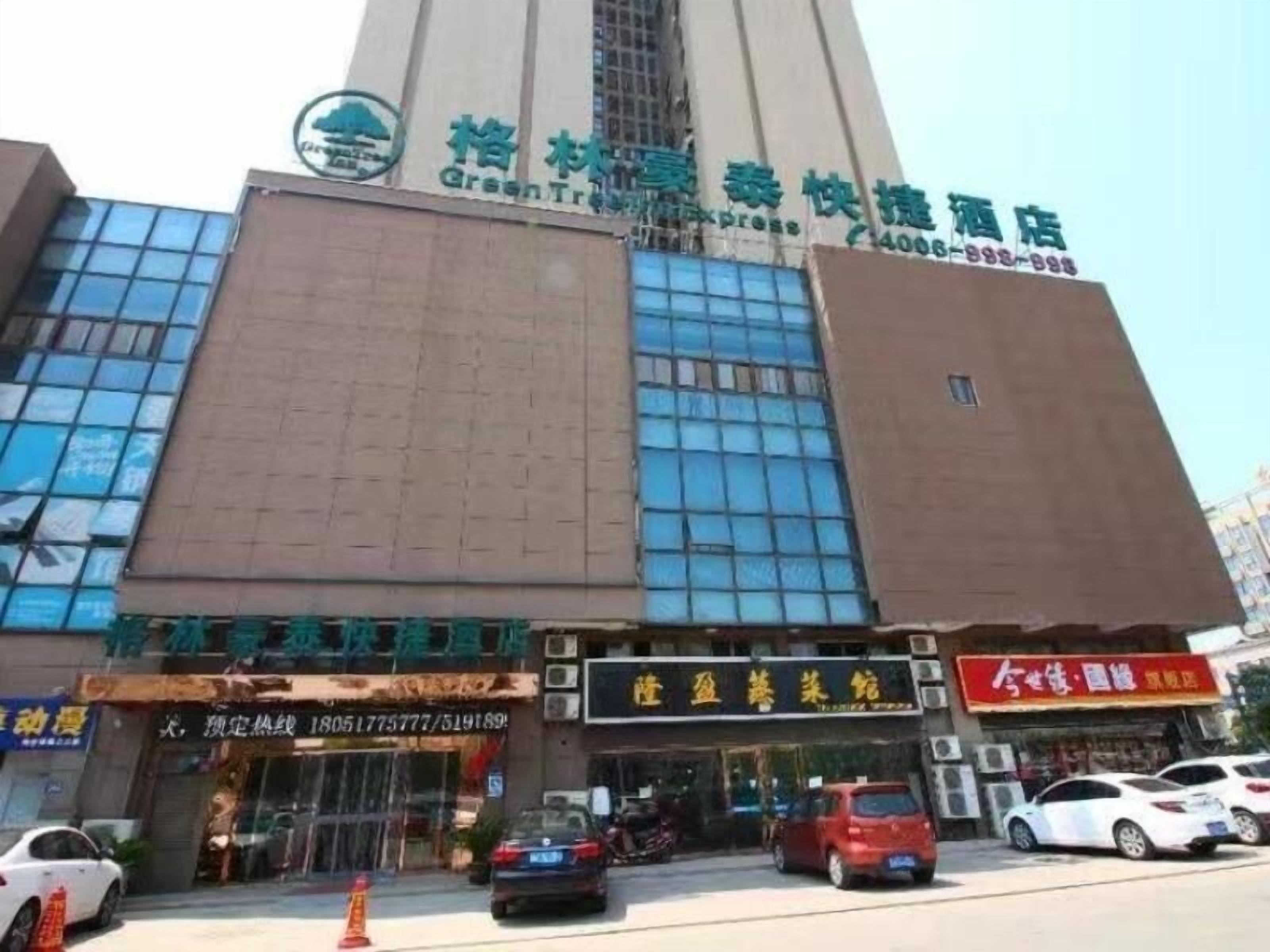A hotel with a prominent green sign, multiple ground-level shops, and a clear view of the street.